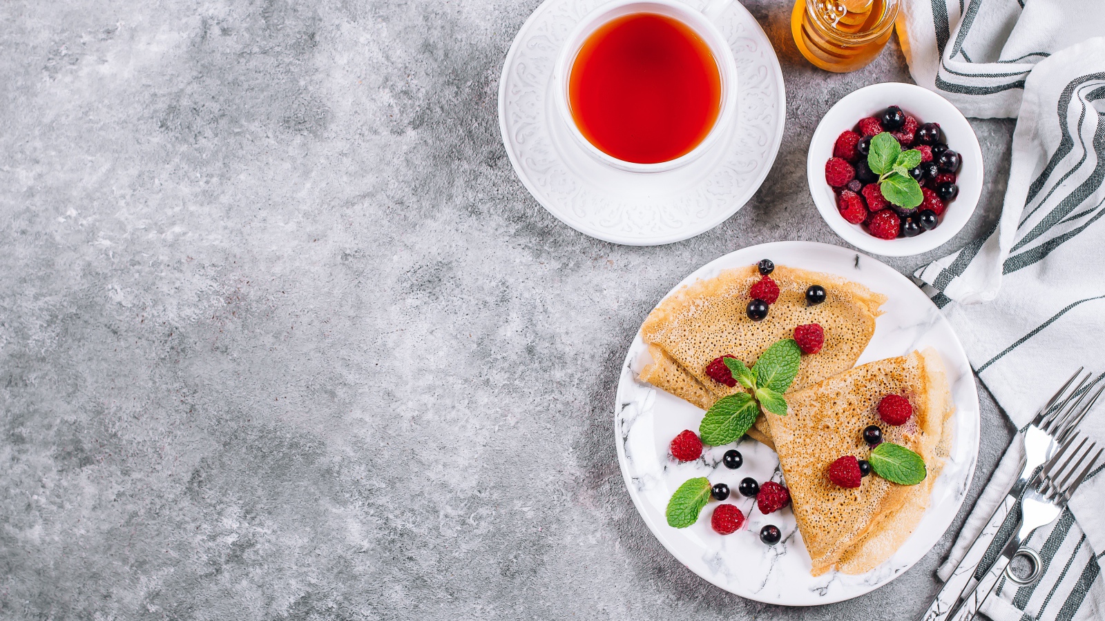 Тонкие блинчики на столе с ягодами, чаем и медом