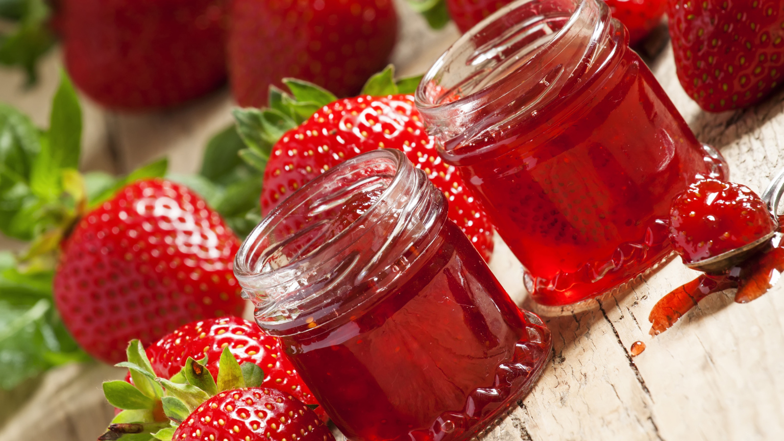 Две баночки клубничного джема на столе с клубникой