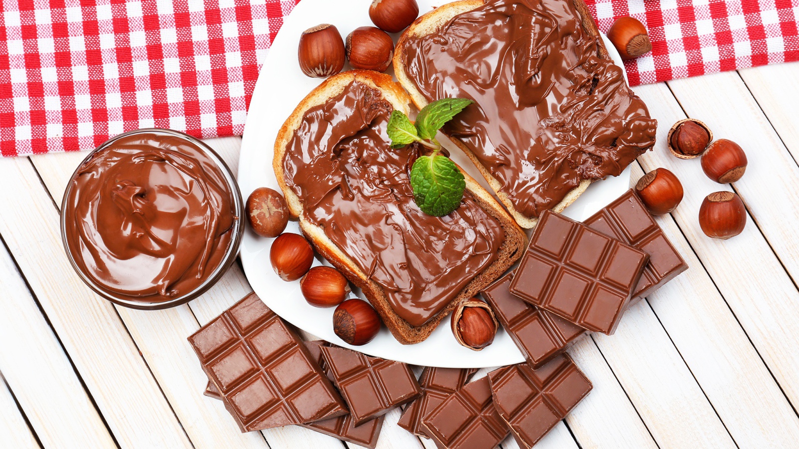 Два куска с шоколадной пастой на столе с шоколадом и орехами