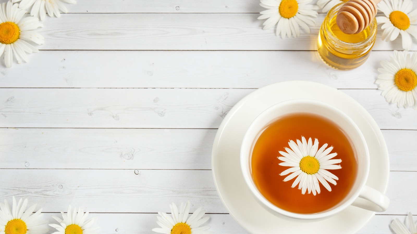 Чашка чая с ромашкой на столе с медом
