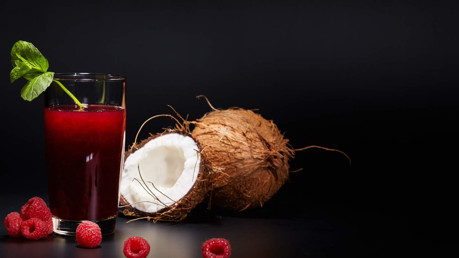 Стакан сока на столе с кокосом и ягодами малины 