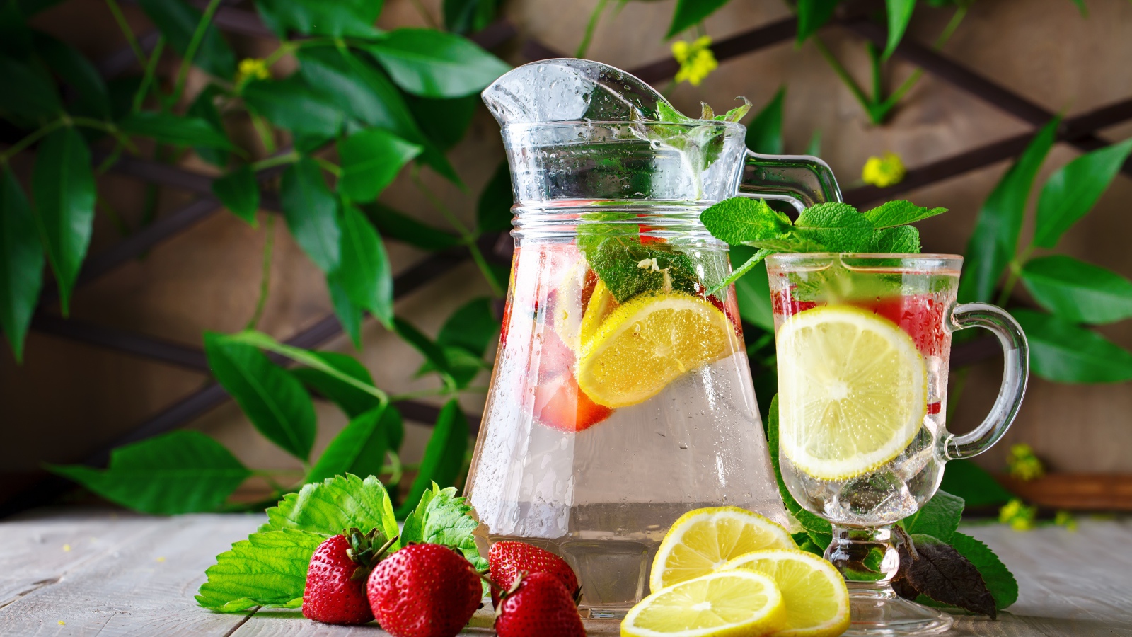 Холодный мохито в графине на столе с клубникой и лимоном