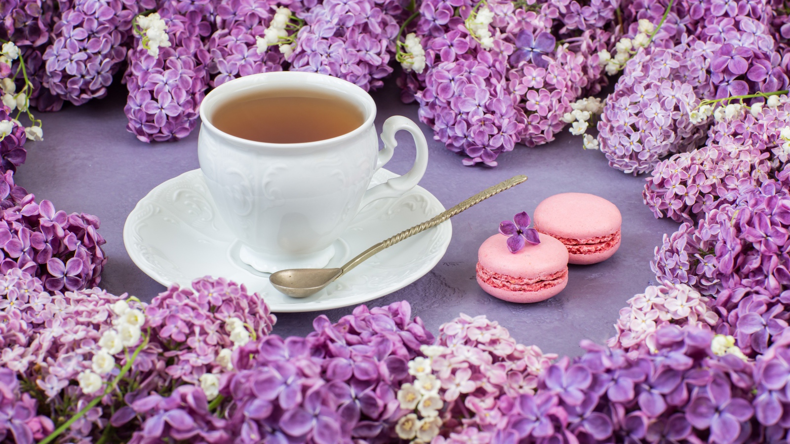 Чашка чая на столе с цветами сирени и десертом макарон