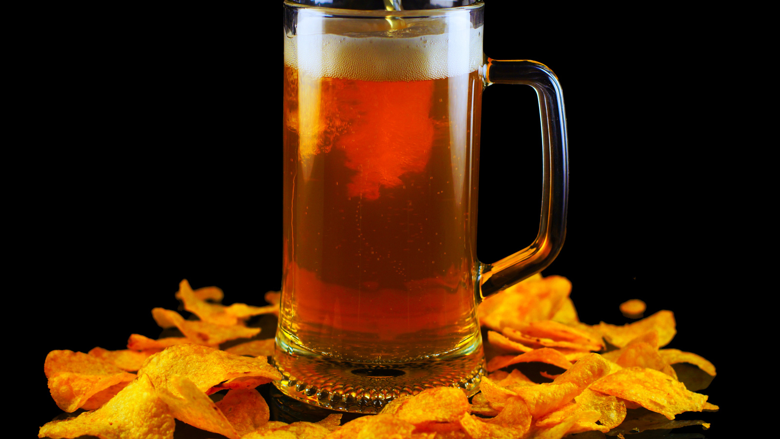 Бокал пива с чипсами на черном фоне