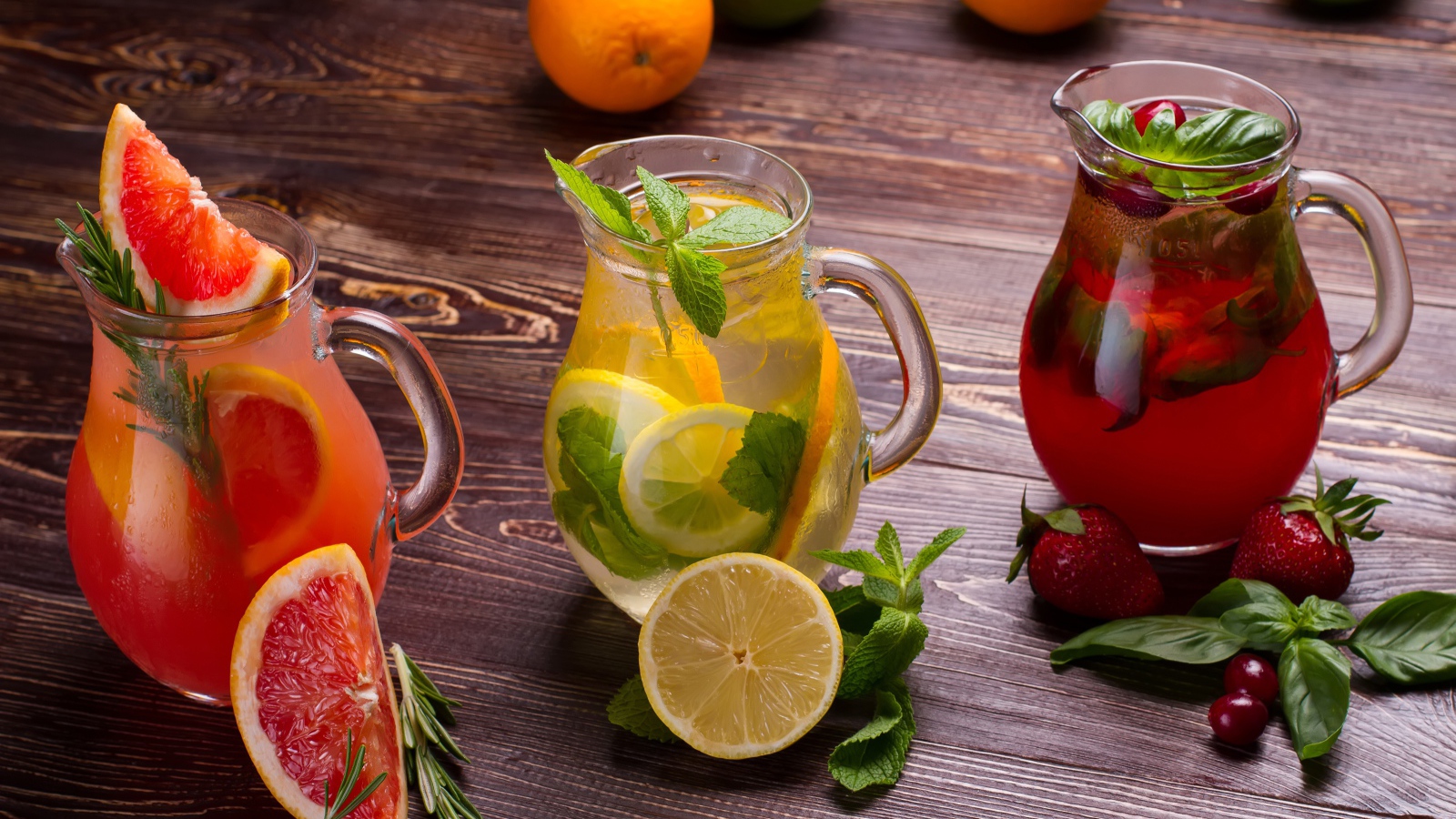 Три стеклянных графина с напитком на деревянном столе с фруктами