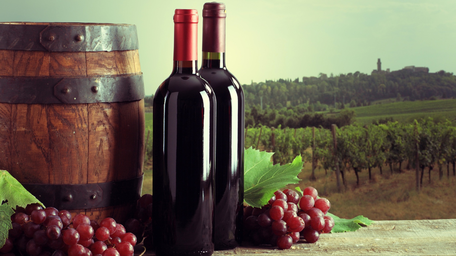 Две бутылки красного вина на столе с виноградом и бочкой