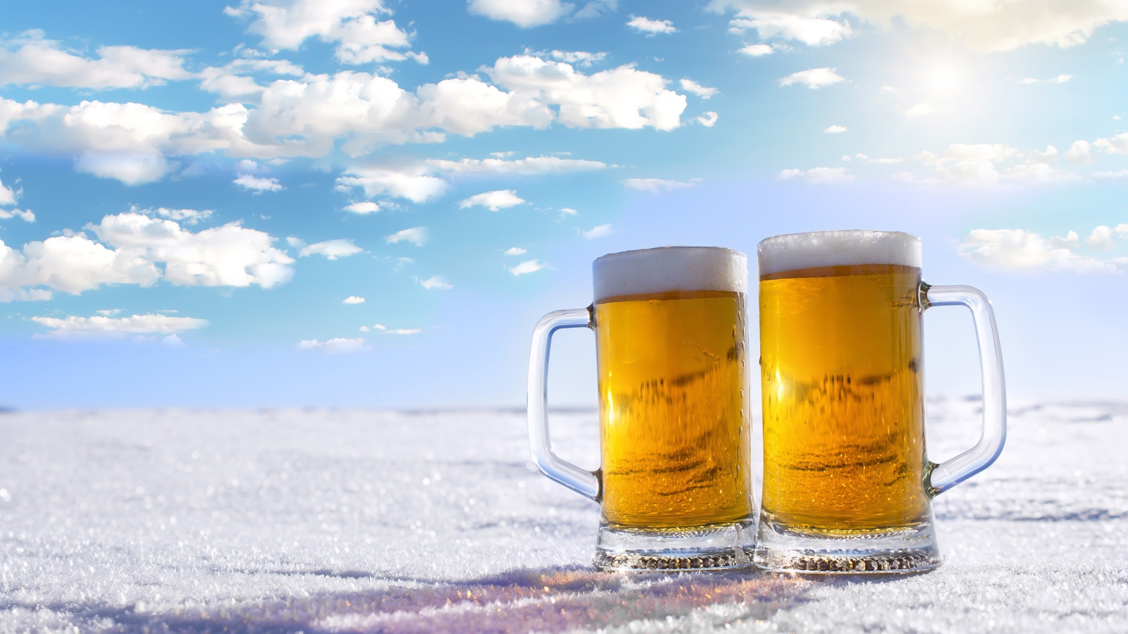 Два бокала пива стоят на белом снегу под голубым небом
