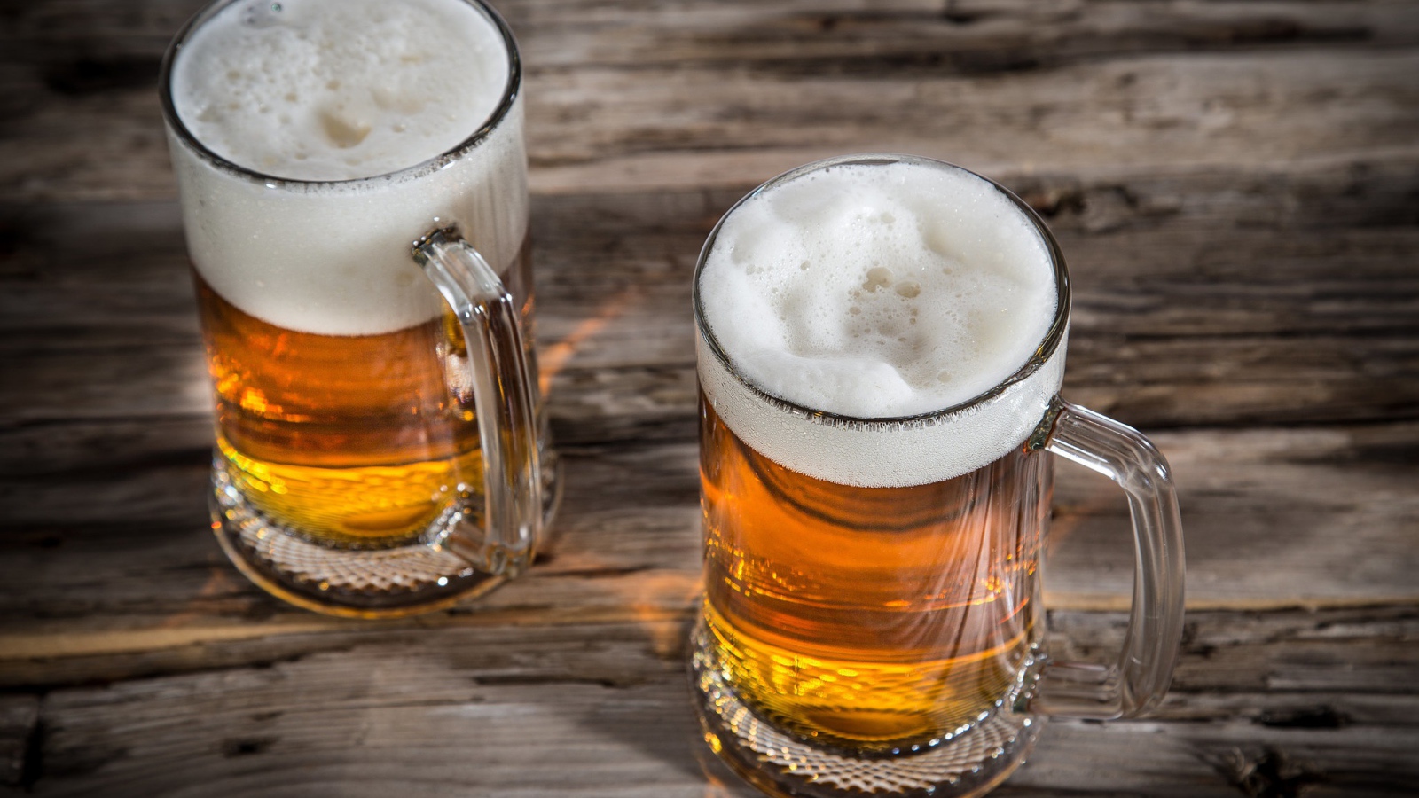 Два бокала пива с пеной на деревянном столе