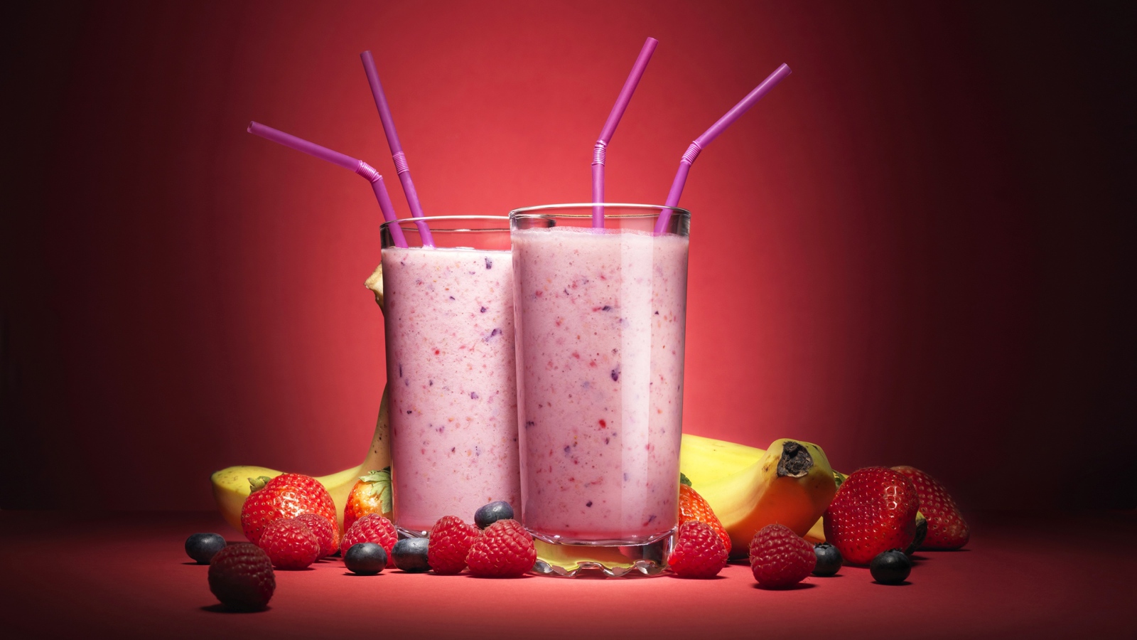 Два стакана смузи на розовом фоне с ягодами и бананами 