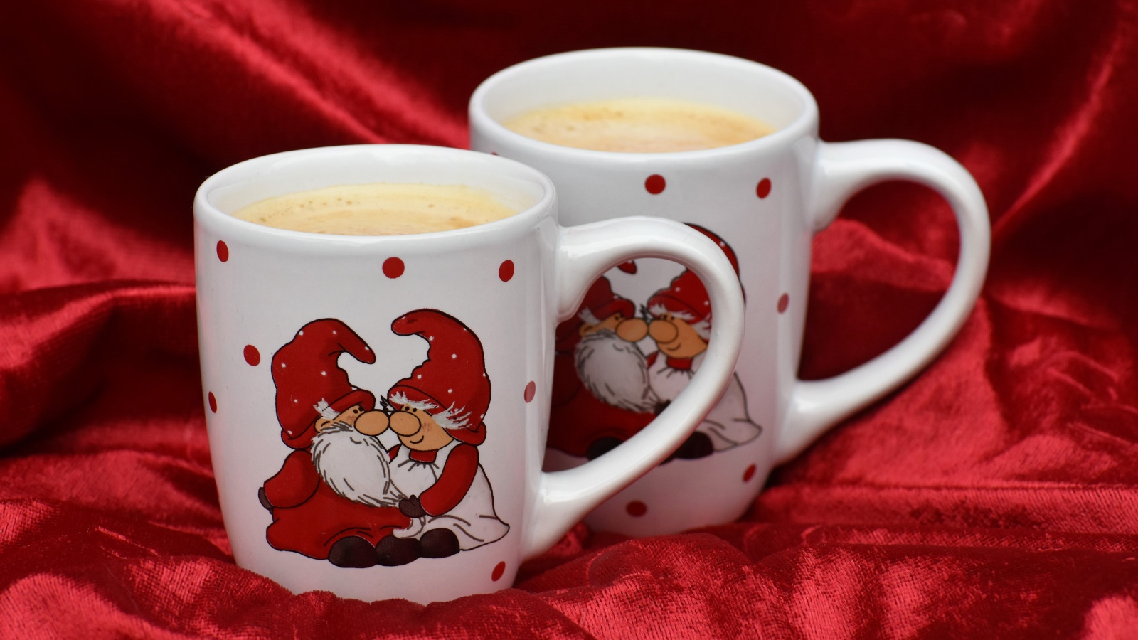 Две белые чашки кофе с рисунком стоят на красной ткани