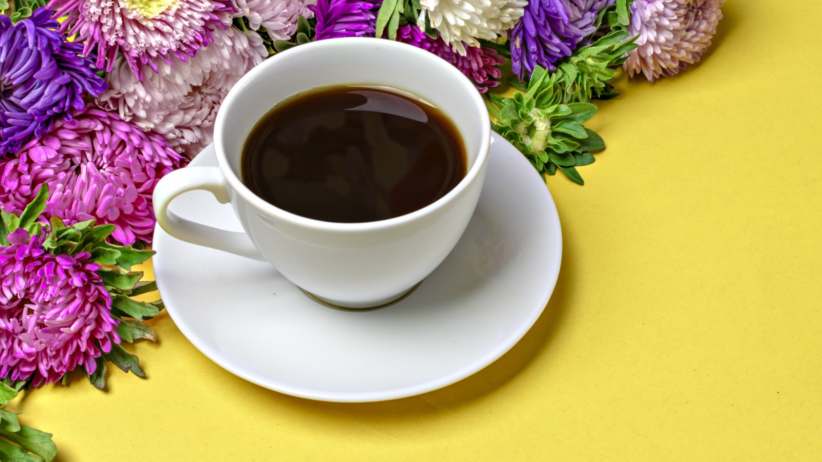 Белая чашка кофе на желтом фоне с букетом цветов астры