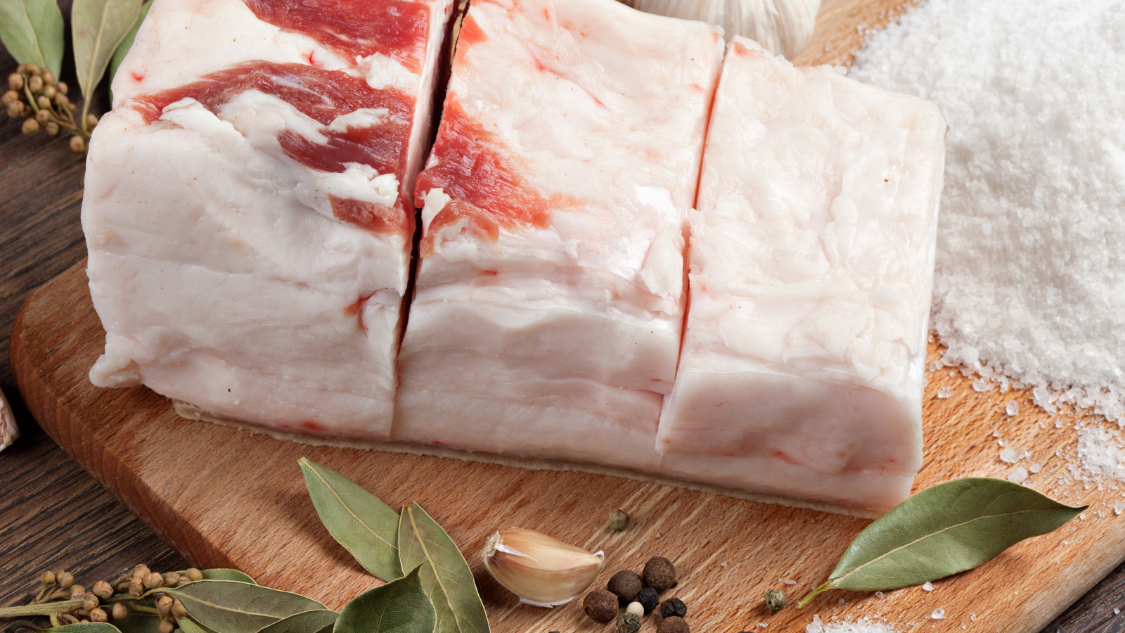 Кусок свежего сала на столе с солью, чесноком и специями