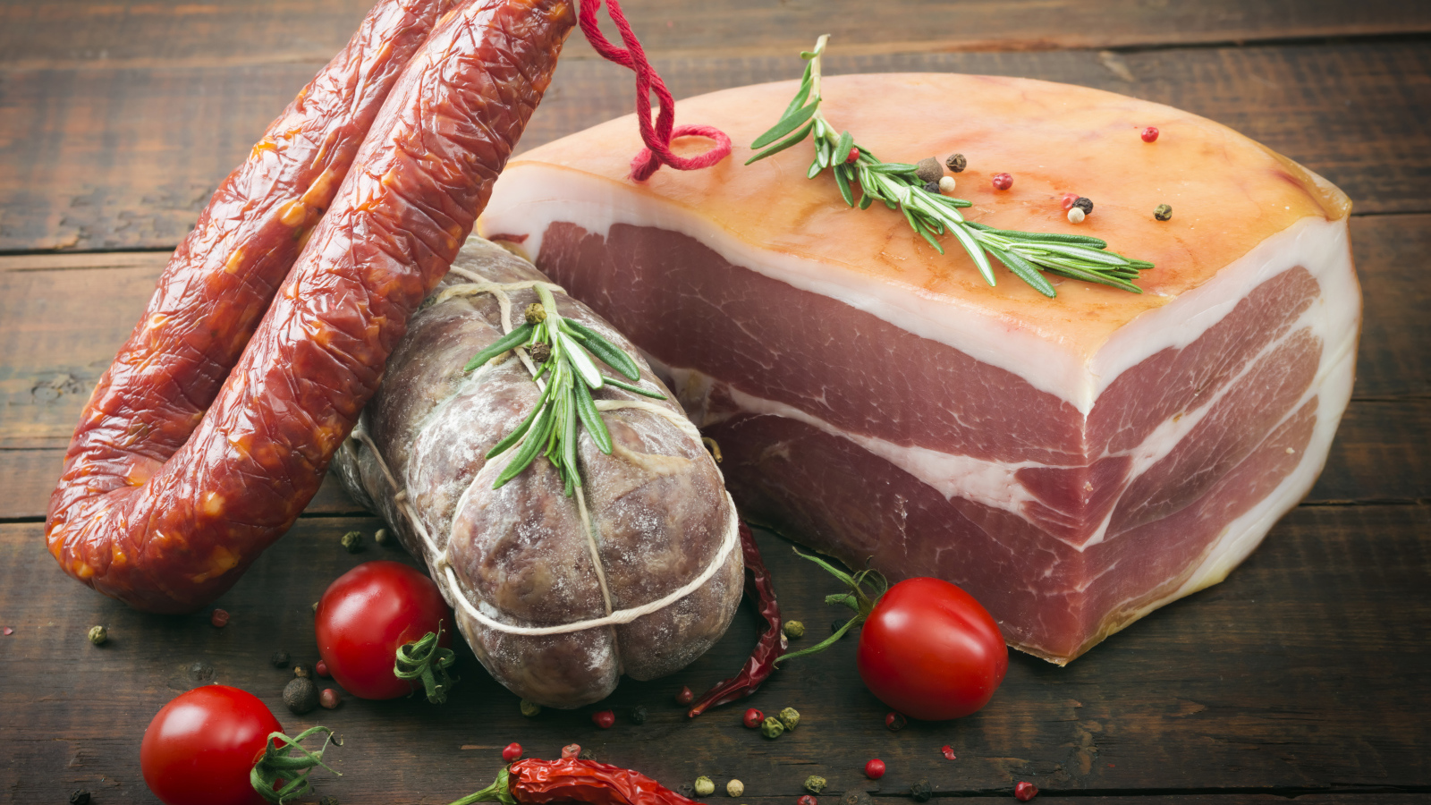 Кусок мяса и колбаса на деревянном столе с помидорами и специями