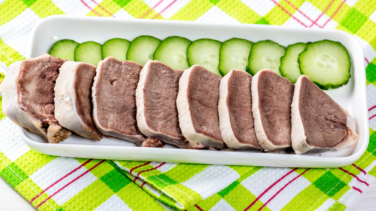 Вареный язык на тарелке со свежими огурцами