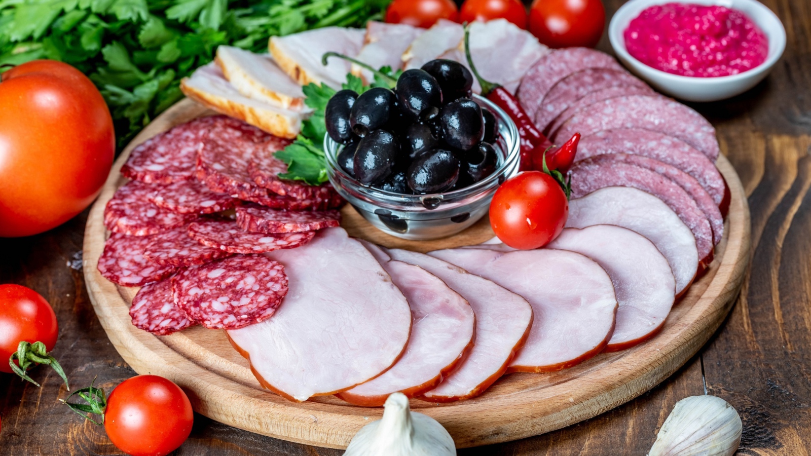 Колбасные продукты на доске с оливками