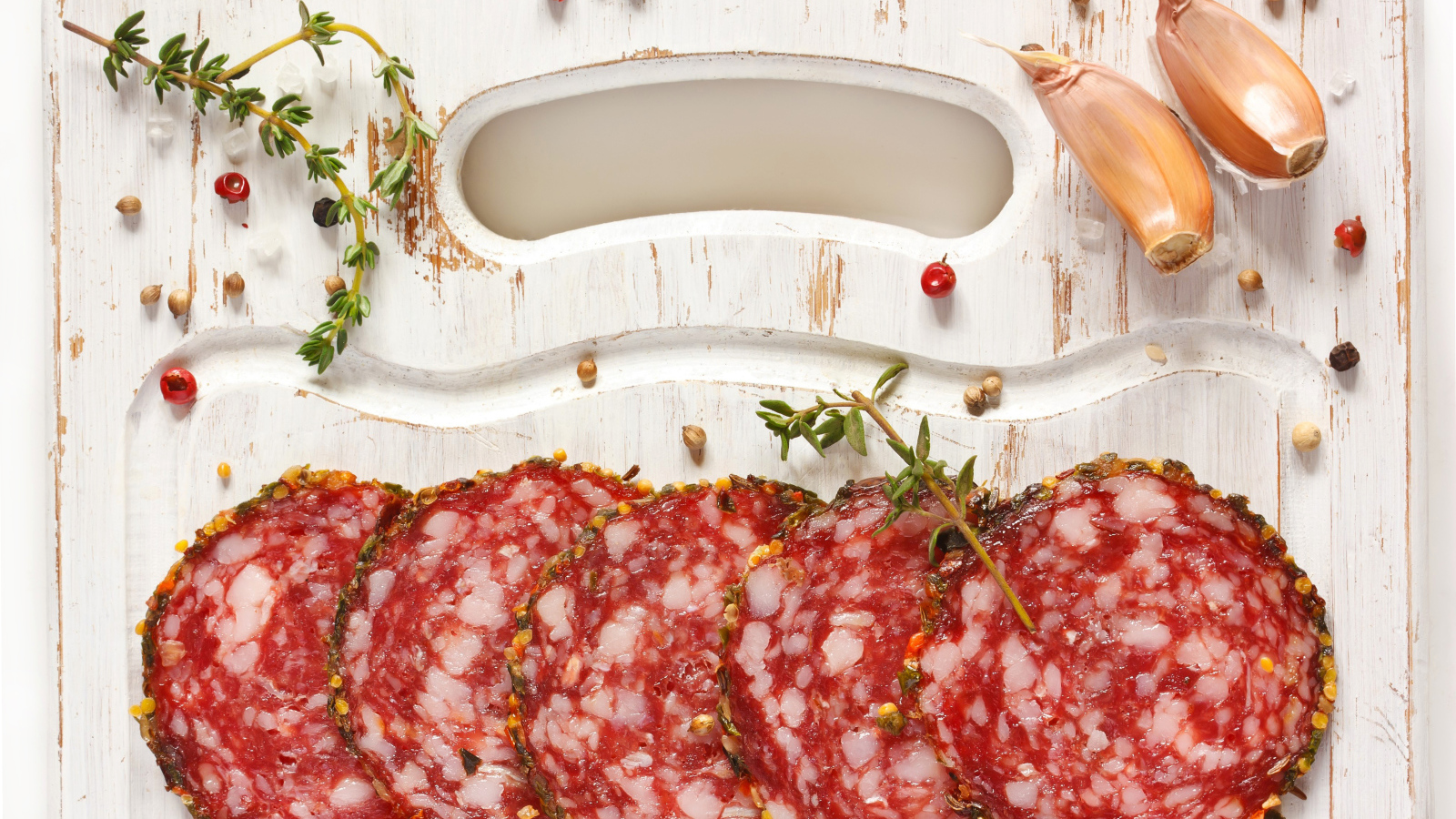 Нарезанная колбаса на разделочной доске со специями и чесноком