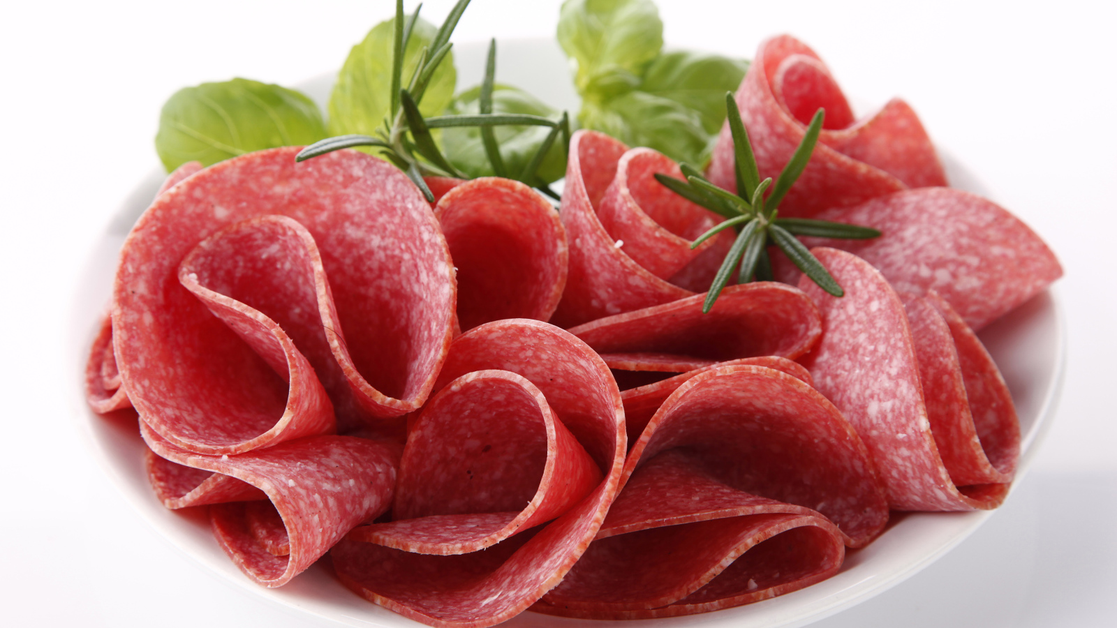 Тонкие кусочки колбасы на тарелке с зеленью 