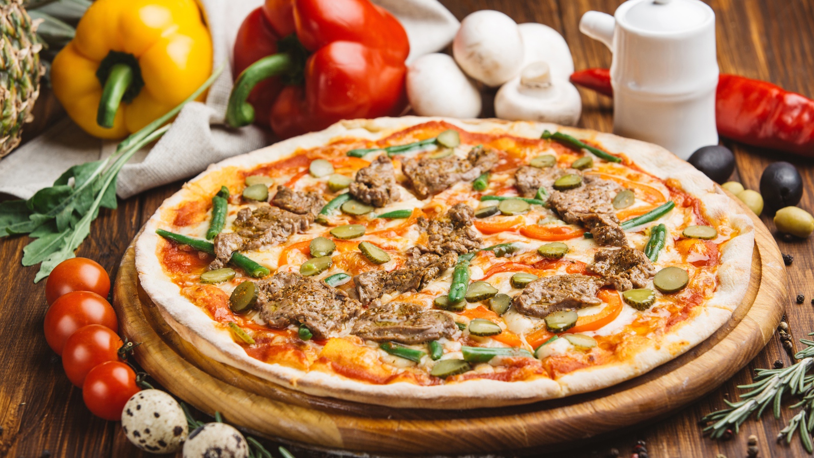 Свежая пицца с мясом и огурцами на столе с овощами