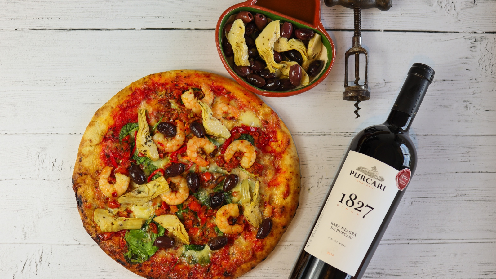 Пицца на столе с оливками и бутылкой вина