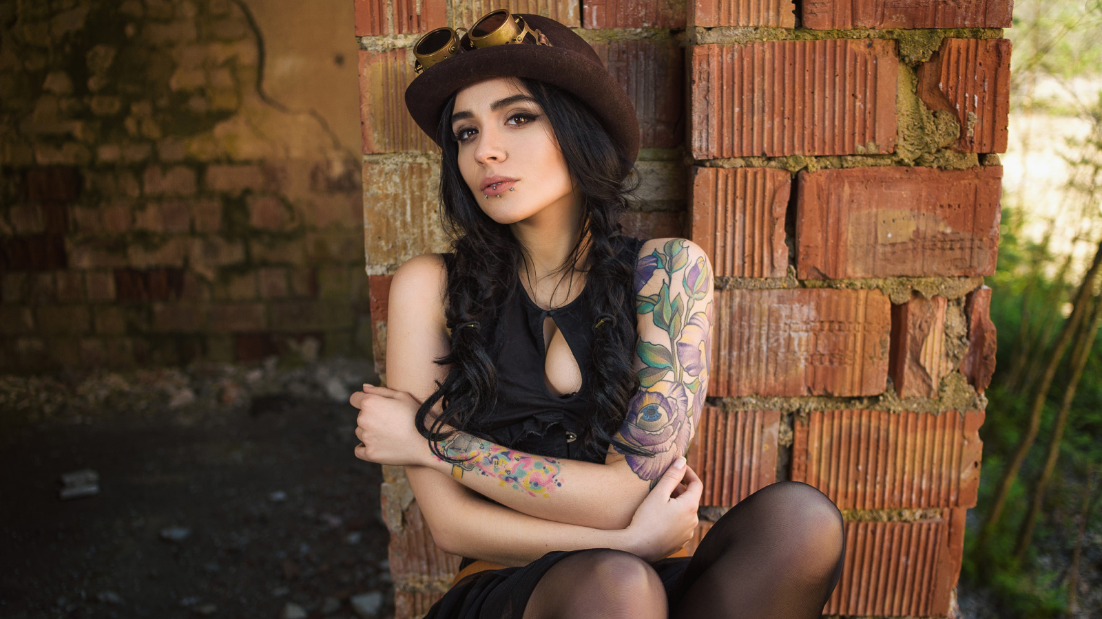 Девушка в шляпе с татуировками на руке сидит у стены