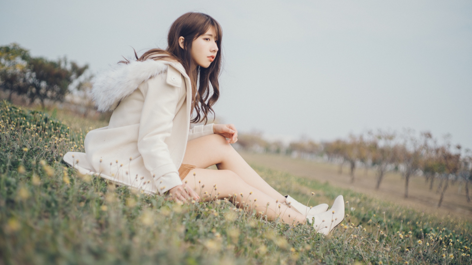 Девушка азиатка в пальто сидит на траве
