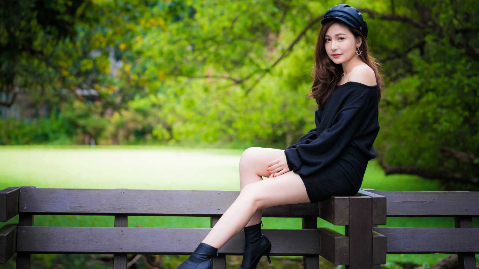 Красивая девушка азиатка в черном платье сидит на деревянной лавке