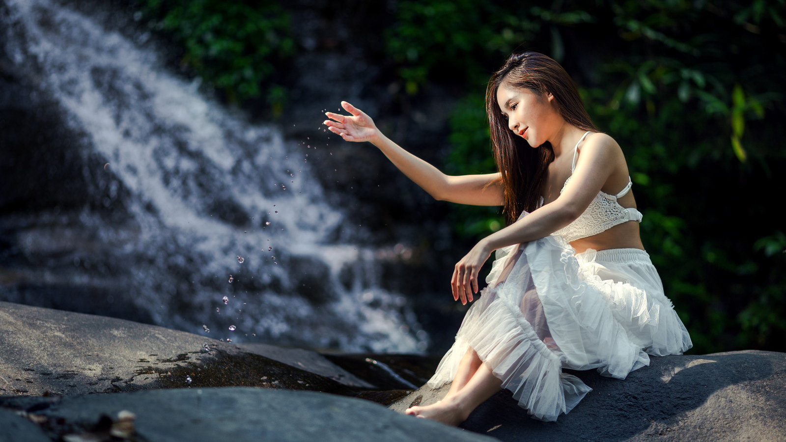 Красивая девушка азиатка в белом платье сидит у воды