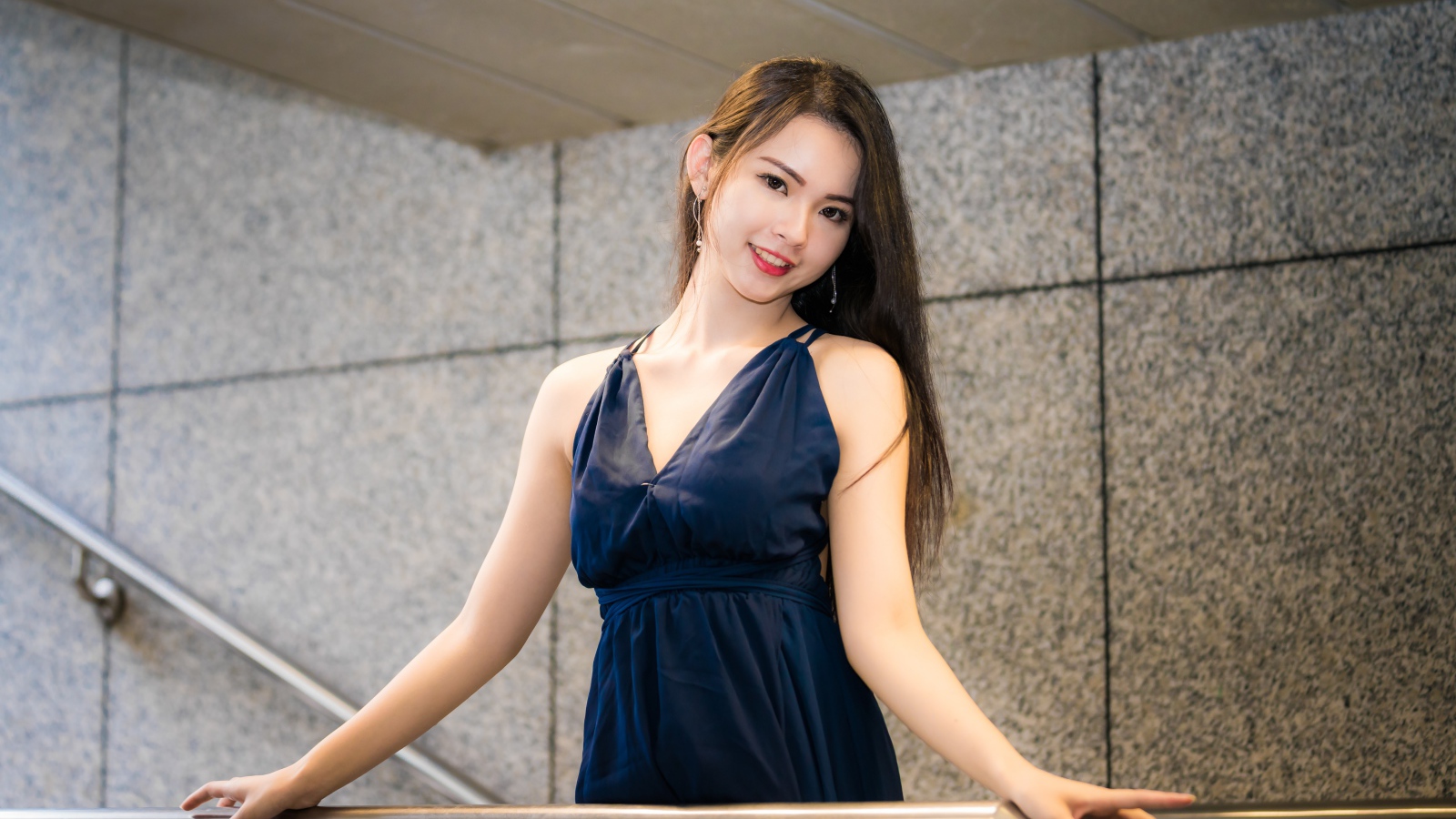 Красивая азиатка в черном платье стоит у перил