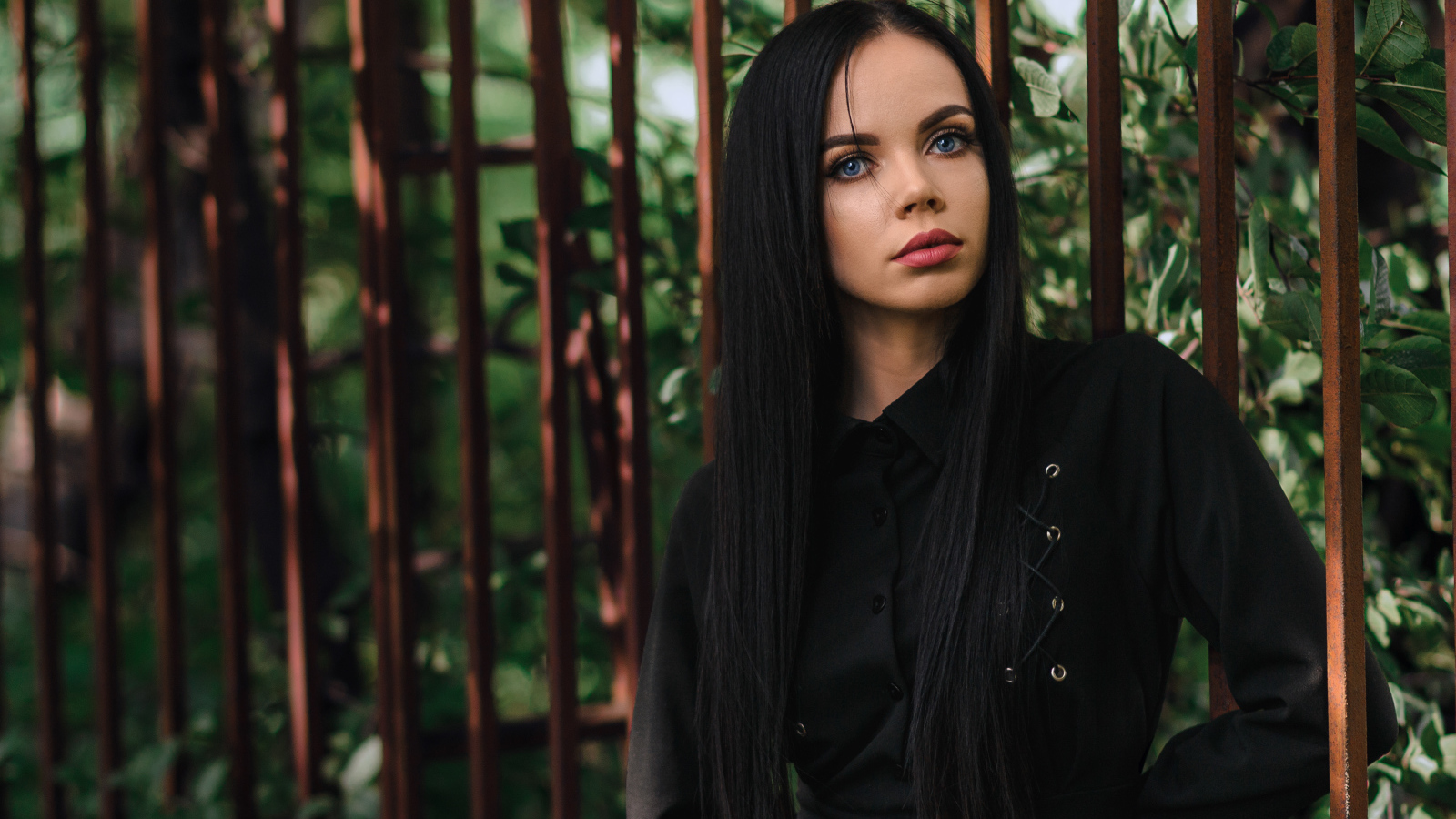 Красивая голубоглазая девушка в черном платье у железного забора