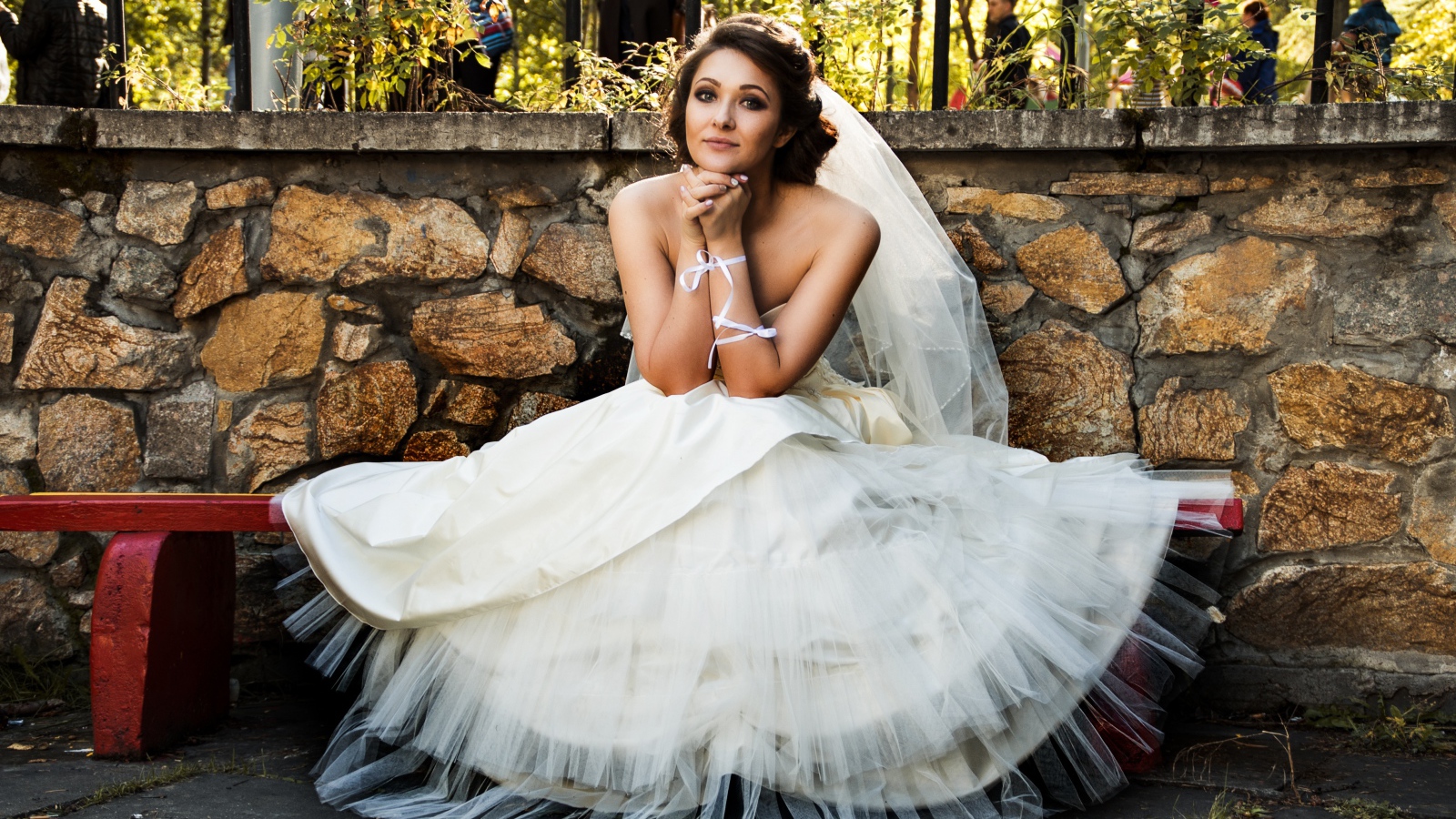 Красивая невеста в белом платье сидит на лавке