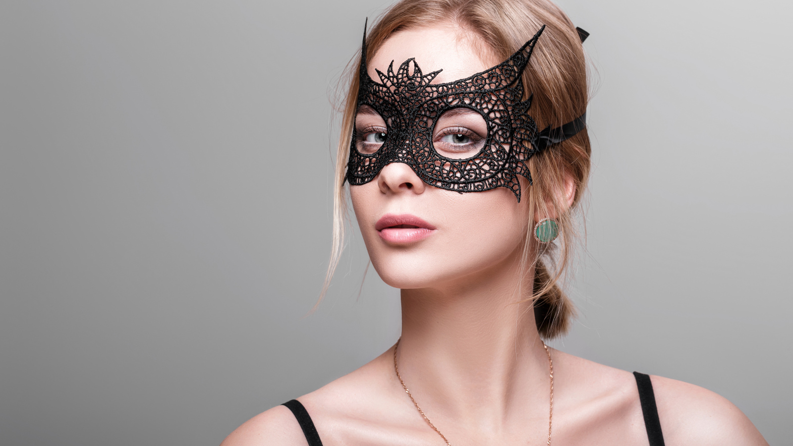 Красивая девушка в черной маске на сером фоне