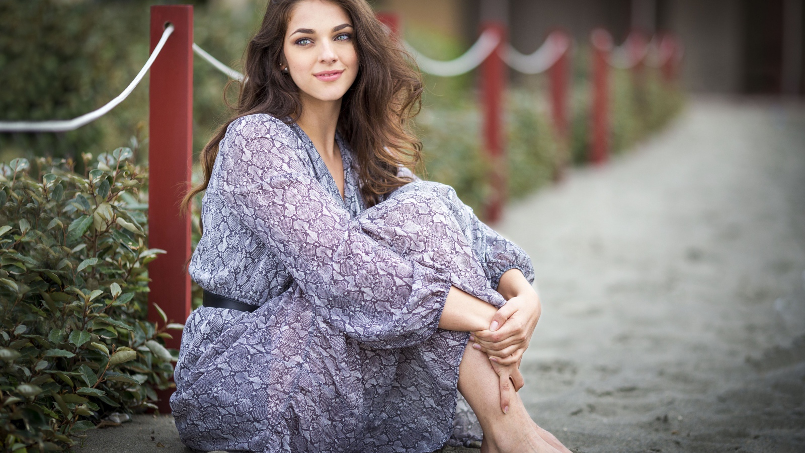 Красивая девушка в платье сидит на песке