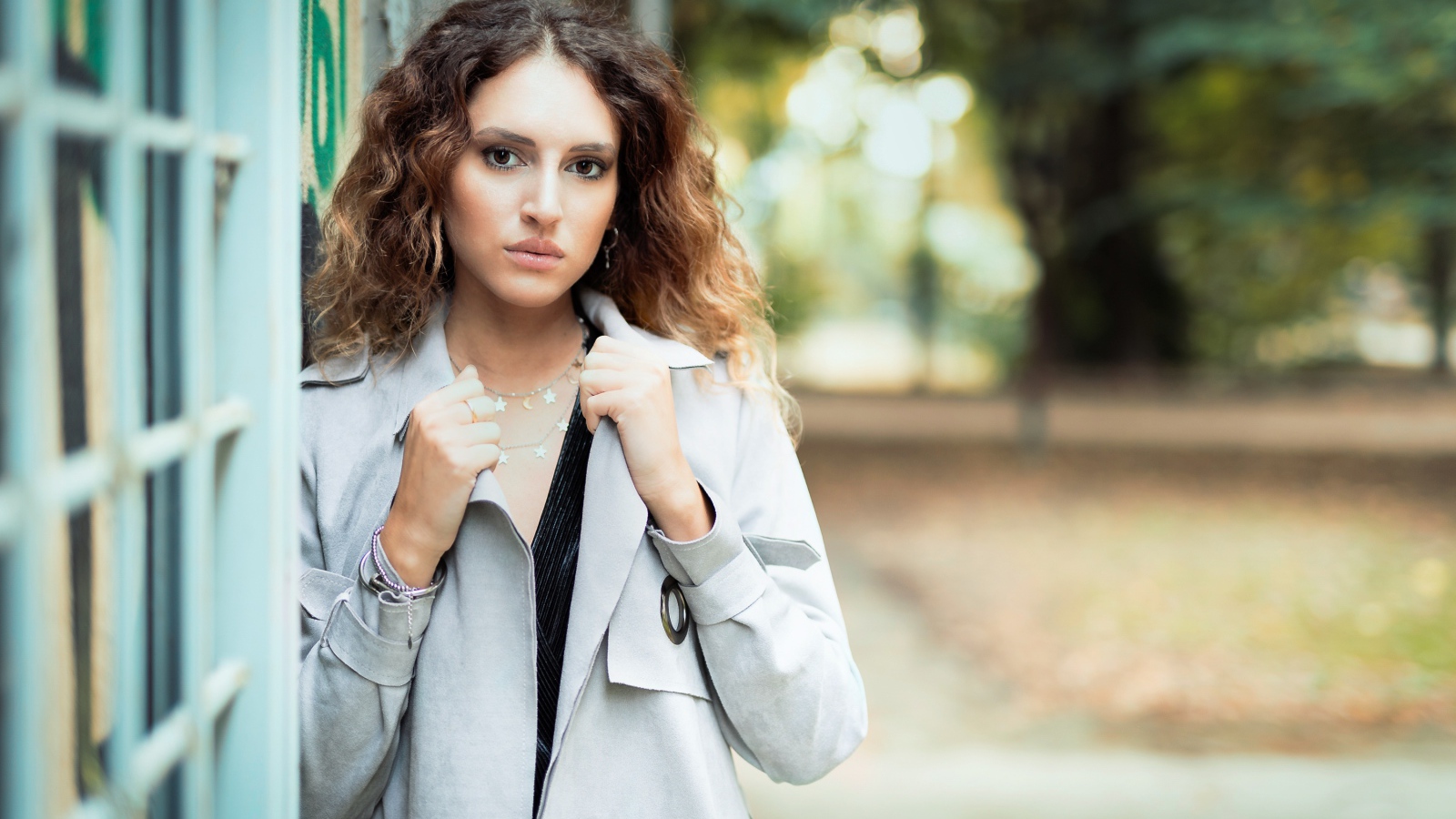 Красивая девушка в сером плаще у стены