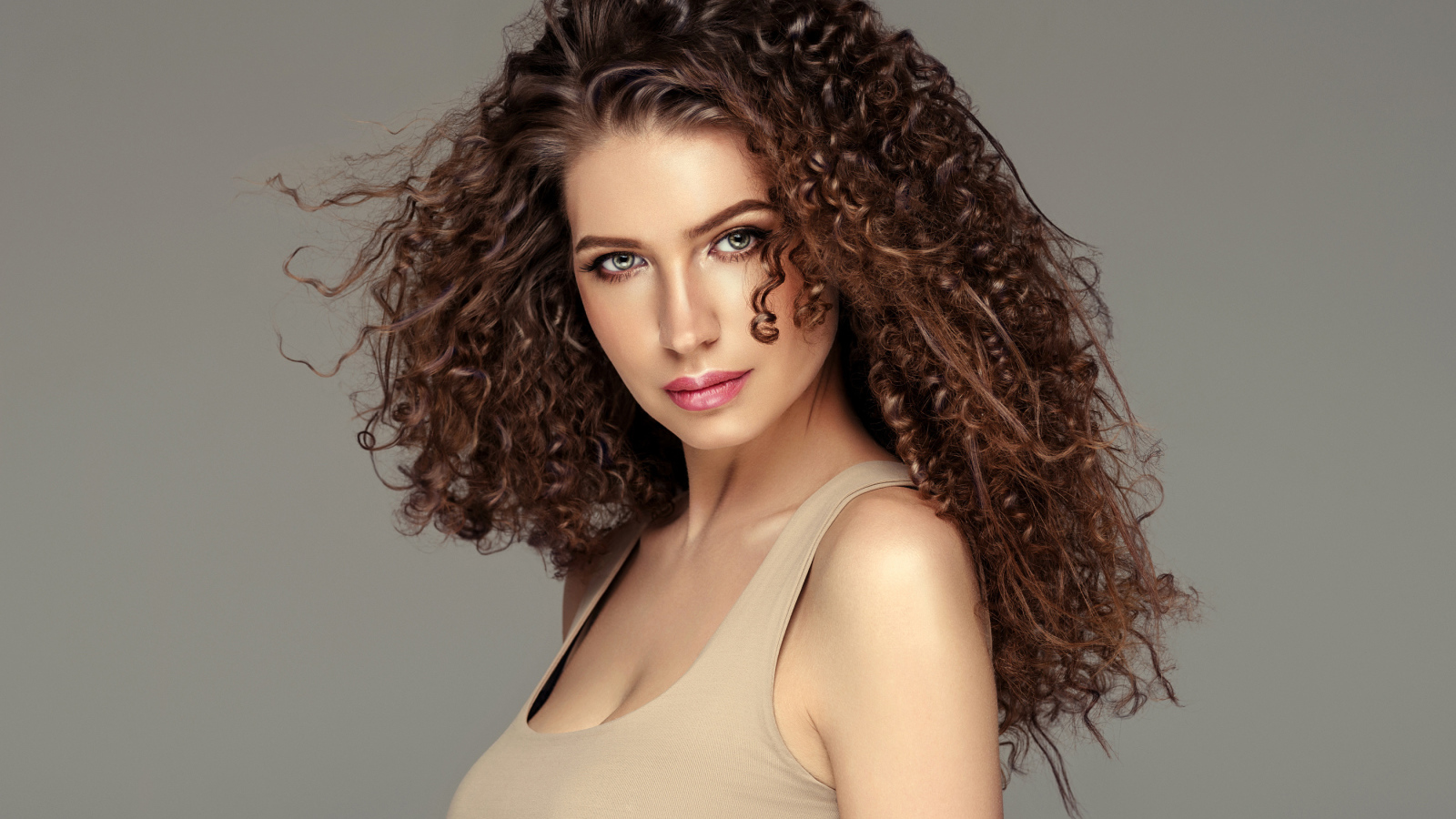 Красивая девушка с накрученными волосами на сером фоне