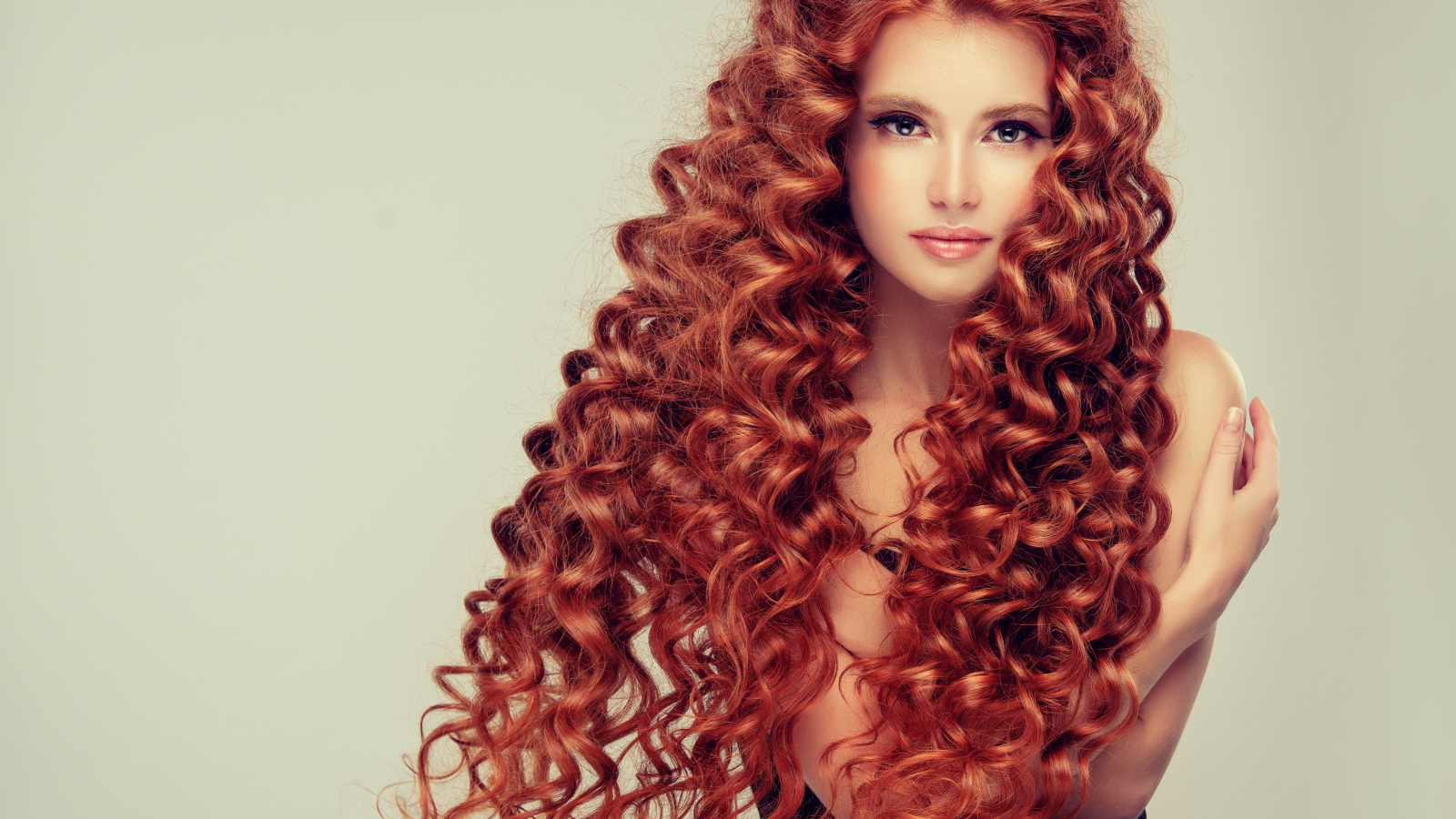 Красивая девушка с длинными рыжими волосами на сером фоне