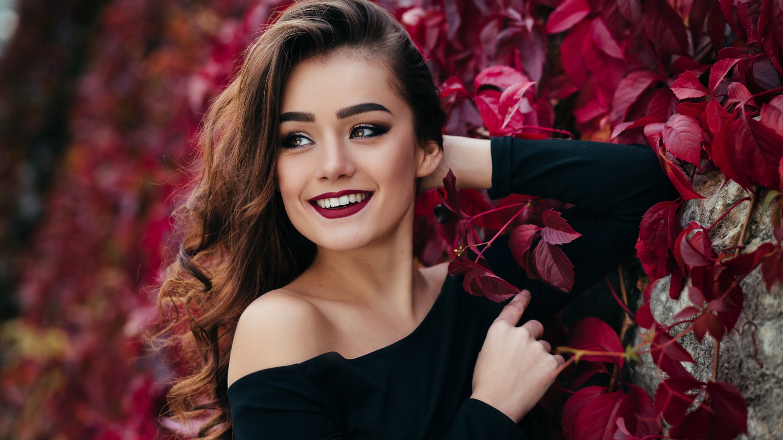 Красивая улыбающаяся длинноволосая девушка у стены с декоративным виноградом