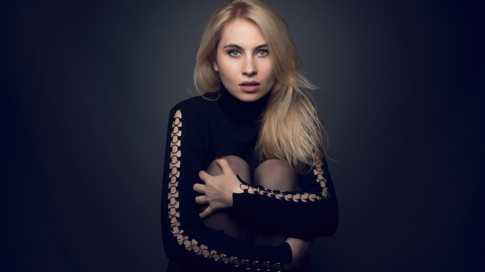 Блондинка в черном наряде на сером фоне