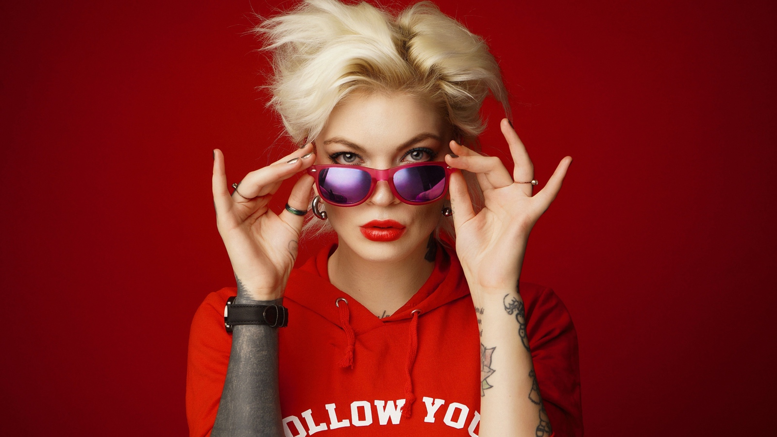 Яркая блондинка с татуировками на руках на красном фоне