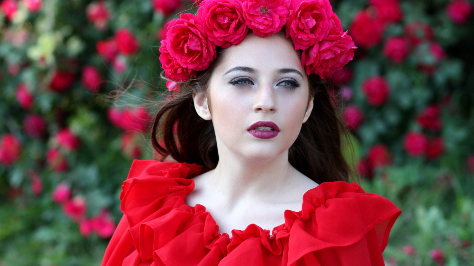 Яркая девушка в красном платье с венком из роз на голове