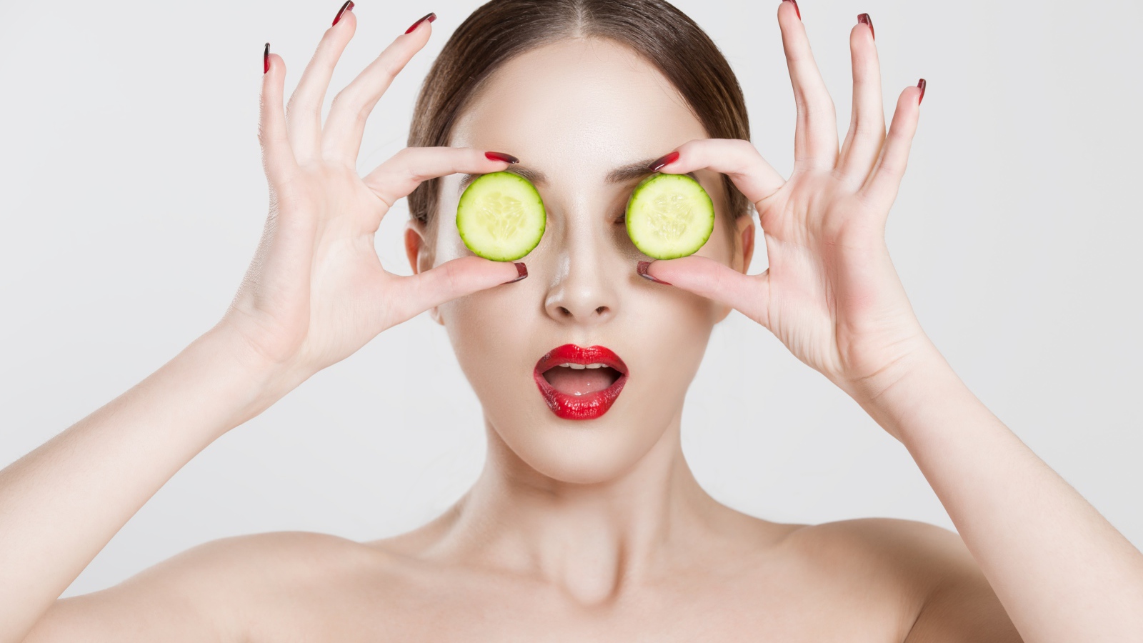Яркая девушка с огурцами у глаз на сером фоне