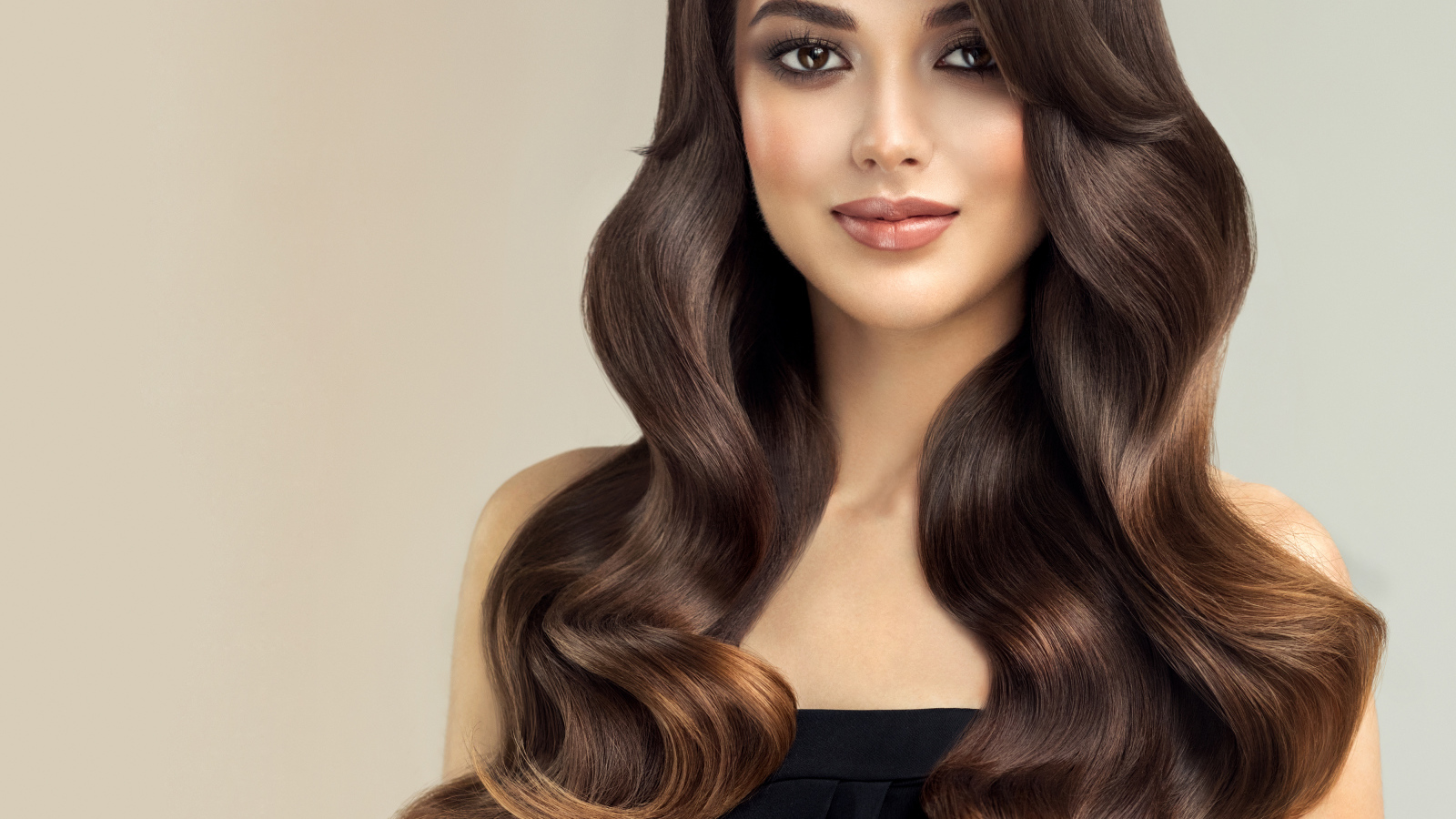 Милая кареглазая девушка с красивыми длинными волосами на сером фоне