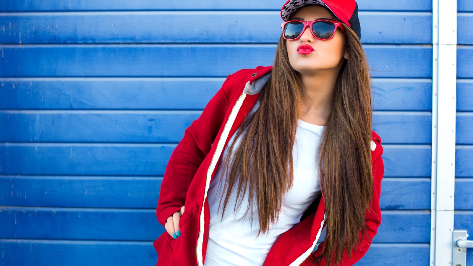 Девушка в бейсболке и солнечных очках у стены