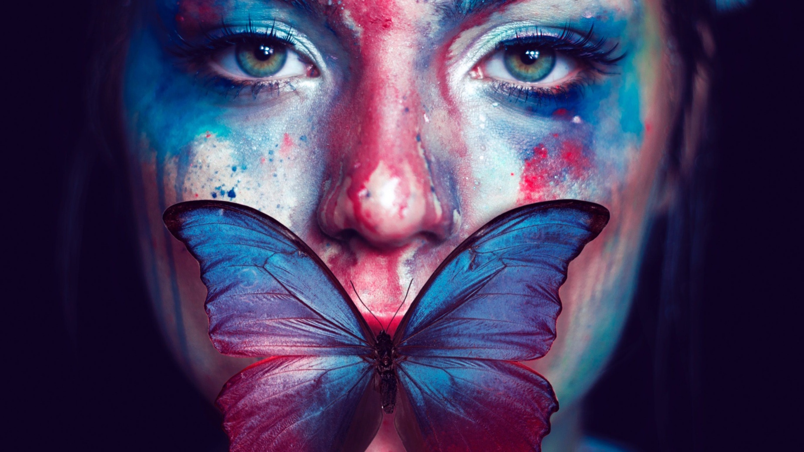 Лицо девушки в краске с бабочкой во рту