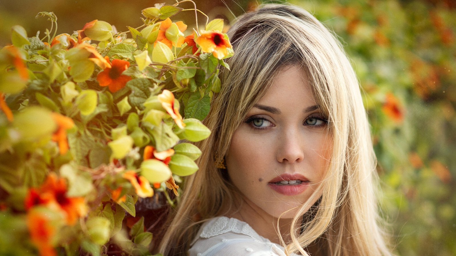 Зеленоглазая блондинка у забора с цветами 