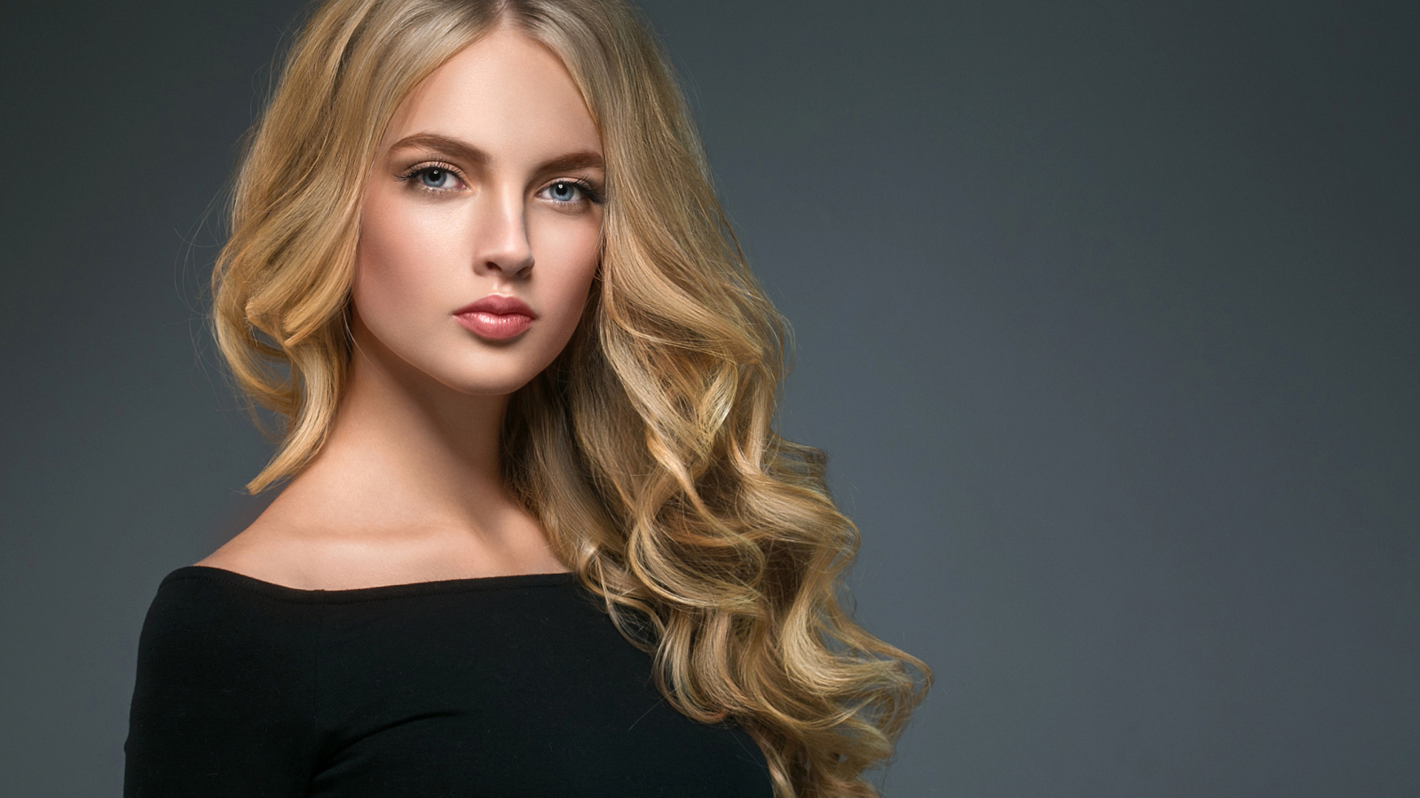 Длинноволосая блондинка с голубыми глазами на сером фоне