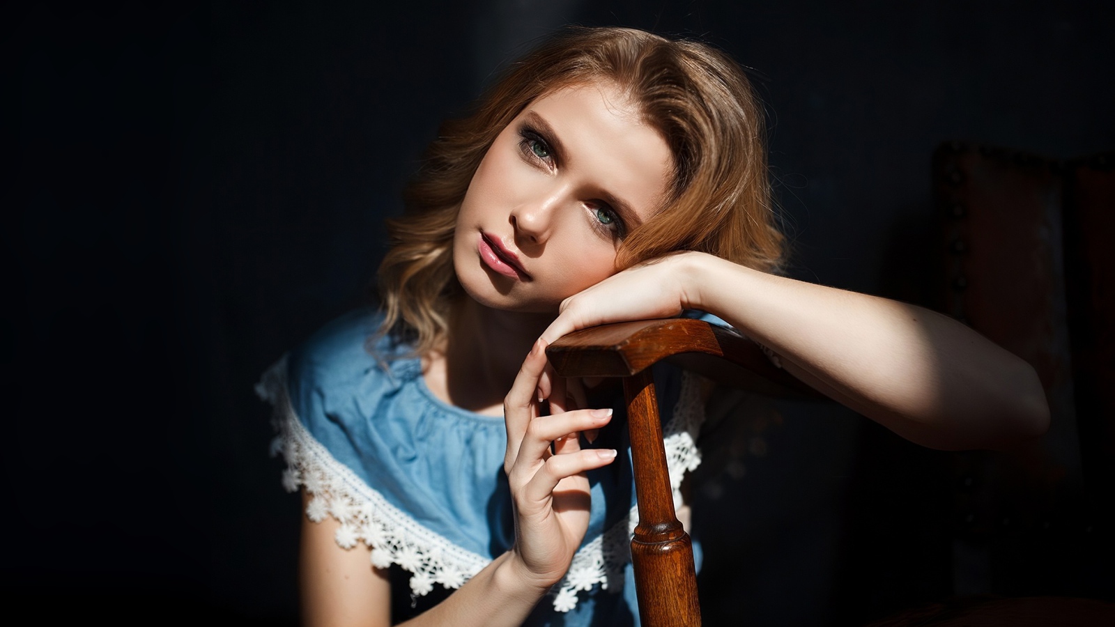 Грустная девушка сидит облокотившись об спинку кресла