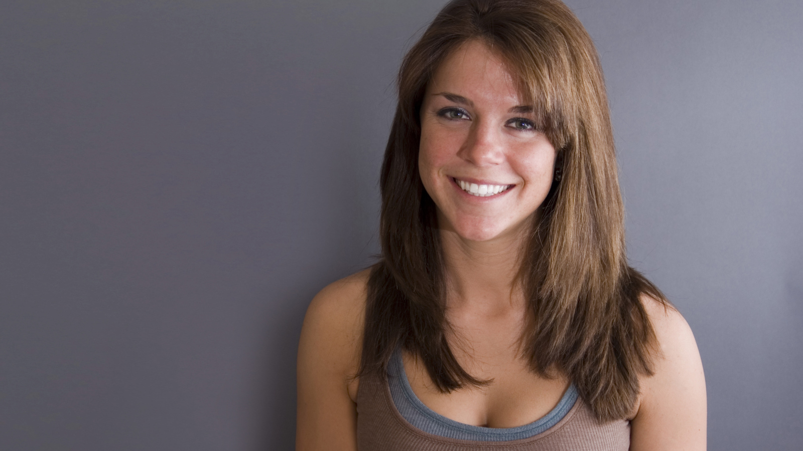 Улыбающаяся милая девушка у серой стены