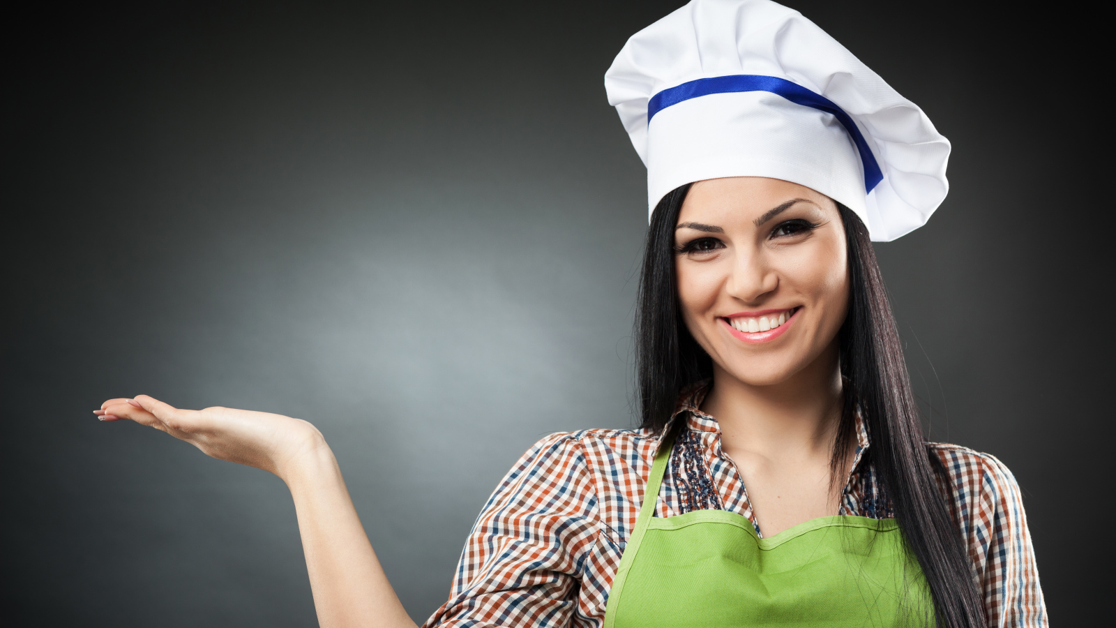 Улыбающаяся девушка в поварском колпаке на сером фоне
