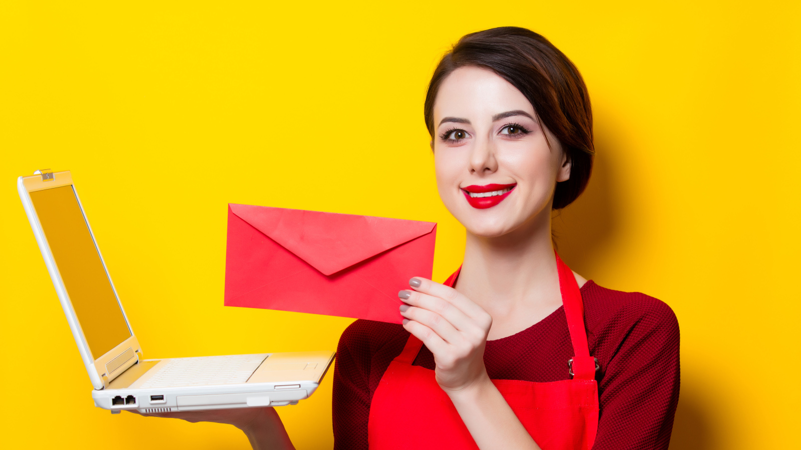 Улыбающаяся девушка с ноутбуком и конвертом в руках на желтом фоне