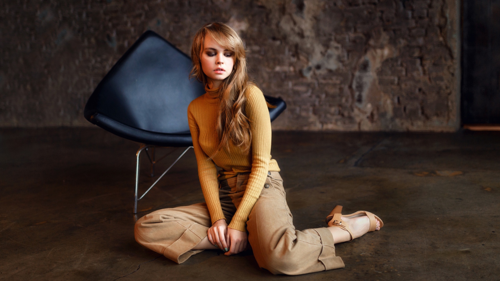 Девушка сидит на полу около черного кресла 